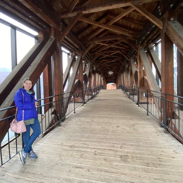 A woman in a blue rain jacket standing inside a covered wooden pedestrian bridge.