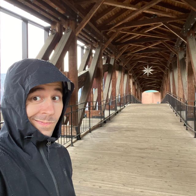 A selfie in a rain jacket inside a covered wooden pedestrian bridge.