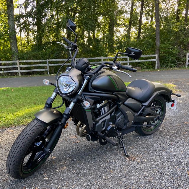 A gray Kawasaki cruiser motorcycle parked beside a wooded road.